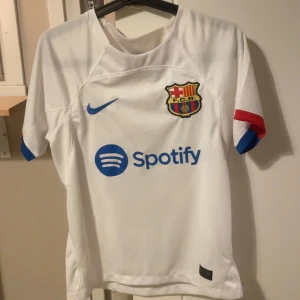 Vit FC Barcelona fotbollströja Lewandowski 9 - Säljer en vit FC Barcelona matchtröja med Lewandowski 9 på ryggen. Tröjan har blå Nike-logga, klubbmärke och sponsortryck på framsidan samt röda och blå detaljer på ärmarna. Materialet är lätt och andas, perfekt för fotboll eller support. Skriv för funderingar eller frågor💯💯💯