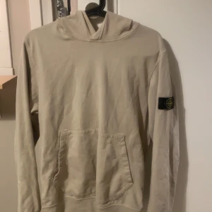 Beige hoodie från Stone Island - Säljer en beige hoodie från Stone Island med klassisk patch på vänster ärm. Tröjan har huva och en stor magficka framtill. Perfekt för en avslappnad stil. Skriv för fler funderingar eller frågor💯💯