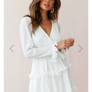 Vit omlottklänning med volangdetaljer - Superfin vit kortklänning med omlott och v-ringning. Långa ärmar och volangdetaljer längs ärmslut och kjol. Perfekt för studenten! Använd fåtal gånger