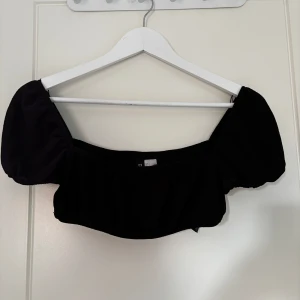 Svart croppad topp med puffärmar från H&M Divided - Säljer en svart croppad topp från H&M Divided med puffiga korta ärmar. Toppen har en fyrkantig ringning och är tillverkad i ett mjukt bomullsmaterial. Perfekt att styla med höga jeans eller kjol.
