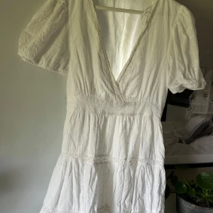 Vit omlottklänning med puffärm - Superfin vit kortklänning med omlott och djup v-ringning. Klänningen har korta puffärmar och markerad midja, samt lätt volang i kjolen. Perfekt för sommarens alla tillfällen!☀️