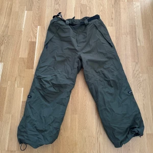 DOPE Mörkgröna täckbyxor med justerbar midja XL - Säljer ett par mörkgröna täckbyxor från dope i XL med justerbar midja och dragsko vid benslut. Perfekta för kalla dagar och utomhusaktiviteter. Byxorna har en loose passform och är tillverkade i syntetmaterial. Endast använda i säsong, levereras såklart nytvättade (fri från doft)