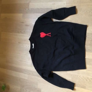 Svart stickad tröja från Ami Paris - Säljer en fet svart stickad tröja från Ami Paris med ett rött hjärta. Klassisk rund halsringning och långa ärmar. Perfekt för dig som gillar stilrena plagg. Säljer då den inte passar. Skriv vid minsta funderingar!