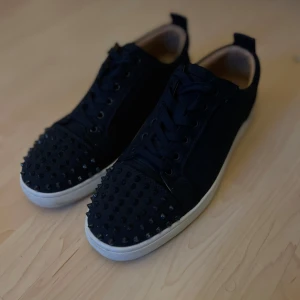 Marin blåa sneakers med nitar från Christian Louboutin - Säljer ett par marin blåa sneakers från Christian Louboutin med blåa nitar på tån. Skorna har vit sula och den klassiska röda undersidan. Perfekta för dig som vill sticka ut med en edgy och lyxig stil.