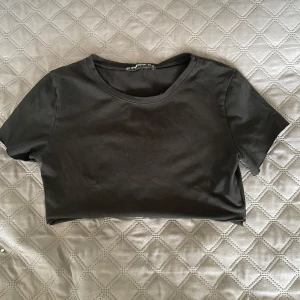 Svart croppad t-shirt  - En enkel svart avklippt t-shirt från Sister i mjuk bomull. Modellen har rund halsringning och korta ärmar, perfekt med en spetströja under. Snygg och stilren baströja som passar till mycket.