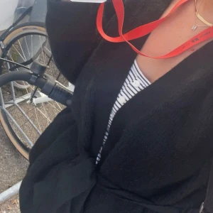 Svart stickad cardigan  - Mysig svart stickad cardigan  med omlottmodell och knytband i midjan. Jackan har lång ärm och en avslappnad passform, perfekt för lager-på-lager. Enkel och stilren design som passar till många outfits.