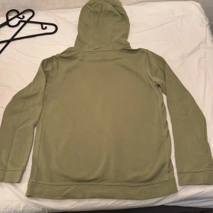 Olivgrön hoodie från Nike - Säljer en olivgrön hoodie från Nike med klassisk logga i vitt och svart på bröstet. Tröjan har huva och en stor magficka framtill. Perfekt för en avslappnad stil och enkel att matcha med jeans eller joggers.