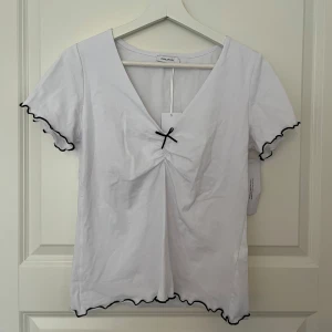 Vit topp med rosett - En vit topp med svarta detaljer! Aldrig använd med lapparna kvar. Toppen har även ett extra lager tyg på framsidans överdel.