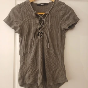 Ribbad olivgrön topp med snörning från Bik Bok - Säljer en ribbad olivgrön topp från Bik Bok med korta ärmar och snygg snörning framtill. Perfekt för dig som gillar en enkel men trendig stil. Toppen har en mjuk och stretchig känsla.
