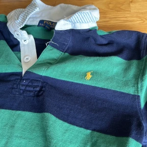 Randig pikétröja från Polo Ralph Lauren - Säljer en klassisk långärmad pikétröja från Polo Ralph Lauren i grönt och marinblått med breda ränder. Nu pris 1,4 tusen