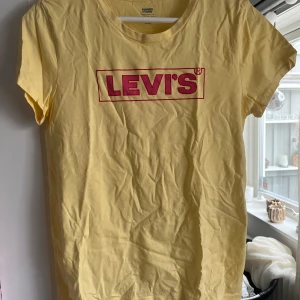 Gul t-shirt från Levi's - Säljer en gul t-shirt från Levi's med klassisk röd logga framtill. T-shirten har rund halsringning och korta ärmar. Perfekt för dig som gillar en enkel och stilren look med en poppig färg. Aldrig använd. Skriv för fler bilder💛