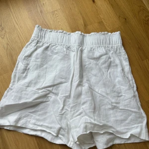 Vita linneshorts  - Säljer ett par vita shorts från H&M i mjukt och svalt linne. De har elastisk midja och en avslappnad passform, perfekta för varma dagar. Klassisk och enkel design som är lätt att matcha med olika toppar. Högmidjade i storlek s! Använda max 2 gånger!