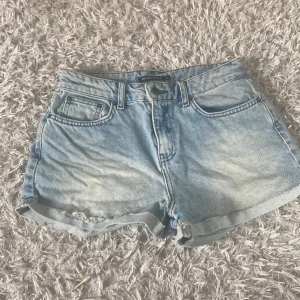Ljusblå jeansshorts från Rut&Circle - Säljer ett par ljusblå jeansshorts från Rut&Circle i klassisk femficksmodell. Shortsen har uppvikta benslut och normal passform, perfekta för varma dagar. Stängs med dragkedja och knapp framtill.