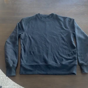 Svart sweatshirt med rund hals - En enkel svart sweatshirt med rund hals och långa ärmar. Tröjan har ribbade muddar vid ärmslut och nederkant. Perfekt för en avslappnad stil.