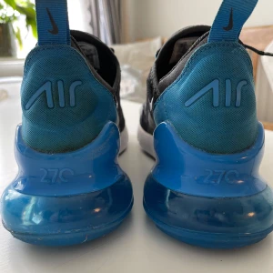 Nike Air Max 270 blå - Nike Air Max 270 sneakers i svart och blått med vit sula och stor blå Air-enhet i hälen. Ovandelen är i mesh med snörning och blå detaljer. Perfekta för dig som gillar sportig stil och vill ha bekväma skor med snygg design. Använd cirka 10 gånger.