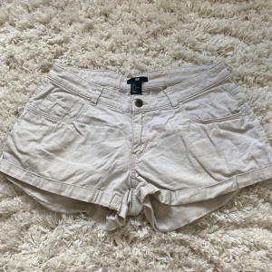 Beiga shorts från H&M - Snygga beiga shorts från H&M med normal passform. De har klassisk femficksdesign, knapp och dragkedja framtill samt uppvikta benslut. Perfekta för varma dagar och enkla att matcha med olika toppar💕