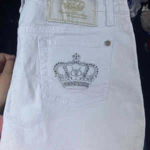  Victoria Beckham kjol - Säljer en vit kjol från Victoria Beckham med en snygg krona i silverbrodyr och strass på bakfickan. Kjolen har klassisk femficksdesign och silverfärgade knappar. Perfekta för dig som gillar exklusiva detaljer. Super snygg äkta Victoria Beckham kjol köpt för typ två år sedan och säljer pga att den är för stor🤍skriv om du har frågor💞