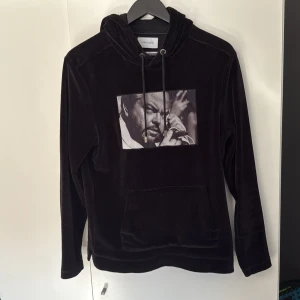 Svart hoodie från Limitato - Säljer en svart hoodie från Limitato i mjuk sammet med ett stort svartvitt tryck framtill. Tröjan har huva med dragsko och en stor magficka. 