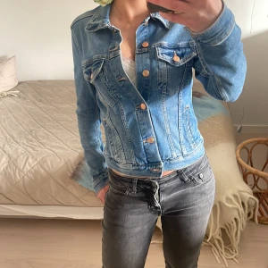 Blå jeansjacka - Säljer en blå jeansjacka med guldfärgade knappar och två bröstfickor. Jackan har en lite smalare passform och är långärmad. Den är även ganska tajt i armarna, fint skick!