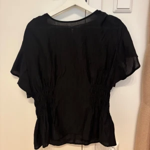 Populär HM blus - Säljer en svart blus med lös passform och resår i midjan. Blusen har korta ärmar och rund halsringning. Perfekt för dig som gillar enkel och stilren design. Populär från HM. 