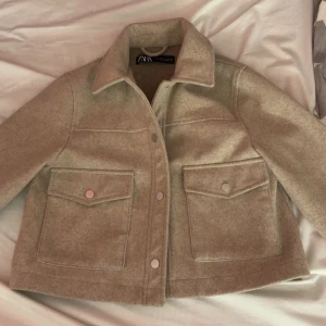 Beige jacka från Zara - Säljer en beige jacka från Zara med klassisk krage och stora fickor framtill. Jackan har knappar och är i ett mjukt material som känns lite ulligt. Perfekt för lager-på-lager och enkel att styla till olika outfits.