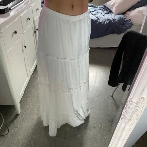 Vit långkjol med volanger från SHEIN - Säljer en vit långkjol från SHEIN i storlek XS. Kjolen har flera lager med volanger och resår i midjan för en bekväm passform. Perfekt för varma dagar och ger en luftig känsla. Materialet är lätt och känns mjukt mot huden.