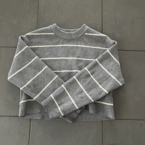 Grå randig stickad tröja från Zara - Säljer en grå stickad tröja från Zara med vita ränder. Tröjan har rund halsringning, långa ärmar och ribbad struktur. Perfekt för dig som gillar en enkel men snygg stil.