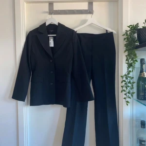 Svart kostymset med kavaj och byxor med prislapp - Kostym set med prislapp nypris 999kr!     Snyggt svart kostymset med klassisk kavaj och raka kostymbyxor. Kavajen har tre knappar framtill, krage. Byxorna är raka i modellen och har hög midja. Perfekt för en stilren och professionell look.