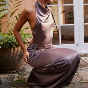 Chokladbrun satinlångklänning från Peppermayo - Elegant brunaktig långklänning i satin från Peppermayo. Klänningen har en draperad hals och öppen rygg. Endast använd en gång, bandet i ryggen är även avklippt så klänningen har helt öppen rygg.🤎