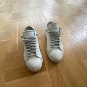 Vita och blå sneakers från Oliver Cabell - Säljer ett par vita sneakers från Oliver Cabell i modellen Low 1. Skorna har ljusblå detalj på hälen och beige mockadetalj på sidan. Klassisk design med snörning och platt sula. Perfekta för dig som gillar stilrena och tidlösa sneakers.