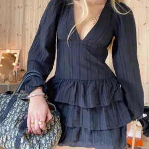 Svart volangklänning från Zara - Supersnygg svart klänning från Zara med lång ärm och djup v-ringning. Klänningen har flera volanglager. Väldigt bra skick!