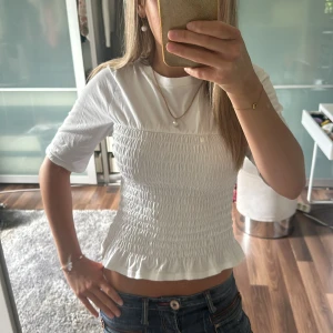 Vit T-shirt från hm - Säljer en söt vit topp med smockad framsida och volangkant nertill. Perfekt till sommaren!🥰🥰från hm, storlek xs