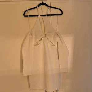 Vit kortklänning med cut out och ringdetalj - Trendig vit kortklänning med lång ärm, cut out-detaljer 