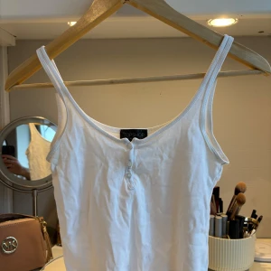 Vit croppad linnetopp från Topshop - Säljer en enkel och fräsch vit croppad linnetopp från Topshop. Toppen har smala axelband och knappar framtill, perfekt för varma dagar eller som layering-piece.