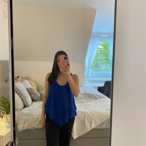 Blå ärmlös linnetopp med volang - Säljer en blå ärmlös linnetopp med volangdetaljer och tunna axelband. Toppen har en lös passform och är perfekt för varma dagar. Enkel och stilren design som passar till mycket.