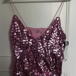 Rosa paljett linne från NLY One - Glittrig rosa topp med smala axelband och v-ringning från NLY One. Helt täckt av paljetter som ger en riktigt festlig look. Perfekt för dig som vill sticka ut och glänsa på nästa event. Aldrig använd, etikett kvar