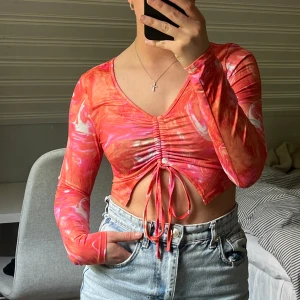 Rosa-orange croppad topp med snöre - Färgglad, somrig topp i rosa och orange med marmorerat mönster. Långärmad modell med v-ringning samt snören att knyta 🩷Frakt tillkommer