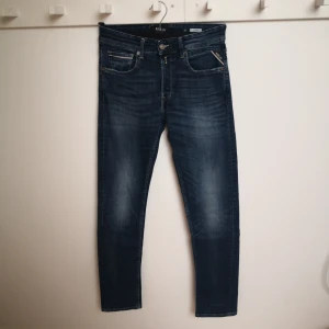 Blå jeans från Replay - Blå jeans från Replay i modellen Grover. De har en klassisk femficksdesign, knappgylf och en bekväm passform. Storlek W 30 L 34. Innerbenslängden ca 87 cm. 