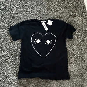 Blå t-shirt med hjärta från Comme des Garçons Play - t-shirt från Comme des Garçons Play med det ikoniska hjärtmotivet med ögon på bröstet. Klassisk passform och rund halsringning. Perfekt för dig som gillar streetwear och vill ha något stilrent men ändå lekfullt. Ny pris 1400 