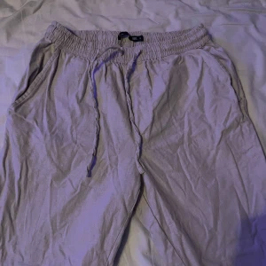 Beige linnebyxor med dragsko - Säljer ett par beige linnebyxor med resår och dragsko i midjan. Byxorna har avslappnad passform, sidofickor fram och två bakfickor. Perfekta för varma dagar och enkel stil.