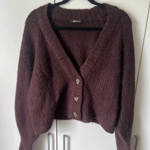 Brun stickad kofta från Gina Tricot - Mysig brun/röd stickad kofta från Gina Tricot med stora knappar framtill. Koftan har en djup v-ringning och långa ärmar. 