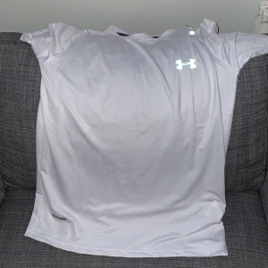 Vit t-shirt från Under Armour - Säljer en vit t-shirt från Under Armour med logga på bröstet. T-shirten har korta ärmar och är tillverkad i ett syntetmaterial som passar perfekt till träning eller sport.