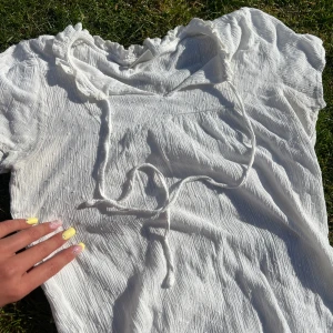 Vit blus med knytband från JDY - Säljer en söt vit blus från JDY i storlek 34. Blusen har korta ärmar, knytband vid halsen och volangdetaljer längs kragen. Materialet är lätt och har en skrynklig struktur som ger en avslappnad känsla.