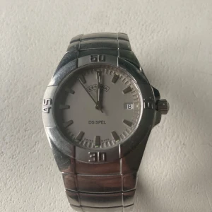 Certina DS Spel herrklocka i silver - Stilren Certina DS Spel herrklocka med silverfärgad länkarmband och vit urtavla. Klockan har datumvisning och tydliga markeringar på boetten. Perfekt accessoar för dig som gillar klassisk design.