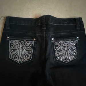 Svarta jeans med broderade bakfickor och strass - Säljer ett par svarta jeans från Miss Me med snygga broderier och strassdetaljer på bakfickorna. Jeansen har en snygg bootcut som inte är för extrem.