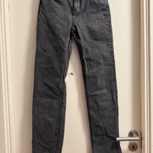 Svarta raka jeans - Säljer ett par svarta jeans med rak passform och klassisk femficksdesign. Jeansen har låg midja och är tillverkade i ett robust denimtyg. Perfekta för en stilren och enkel look.