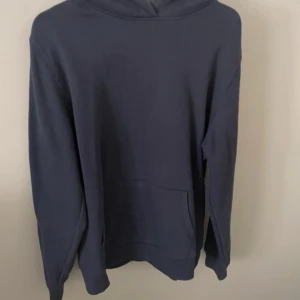 Mörkblå hoodie - Säljer en stilren mörkblå hoodie med långa ärmar och en klassisk känguruficka framtill. Perfekt för en avslappnad look.