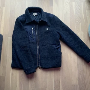 Svart fleecejacka från Morris - Säljer en snygg svart fleecejacka från Morris. Jackan har en dragkedja framtill och en liten broderad logga på bröstet. Perfekt för kyligare dagar med sin mjuka och varma design.