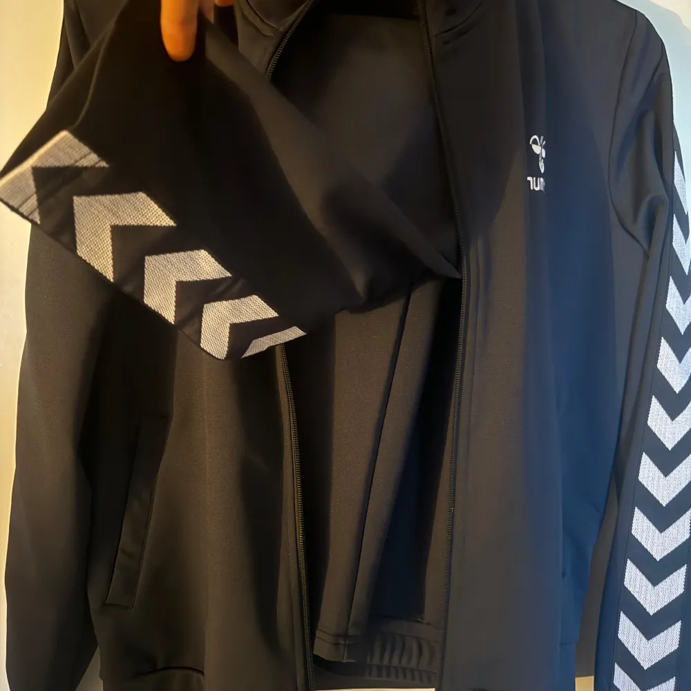 Två svarta träningsjackor, en från Hummel med vita chevronmönster på ärmarna och en från Adidas med klassiska ränder. Båda har dragkedja och långärmade design. Perfekta för sport och vardag. S-M två för 400kr 300kr/st. Takit.