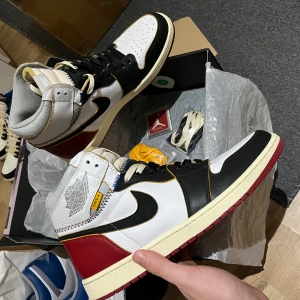 Jordan 1 High Union LA - Snygga Nike Air Jordans med en klassisk design i svart, vitt och rött. Skorna har snörning och en hög siluett med ikoniska detaljer. Perfekta för sneaker-entusiaster som vill ha en stilren look.